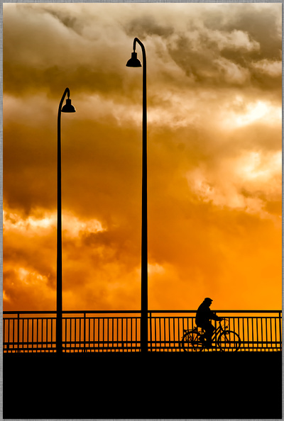 ﻿Fahrradfahrer mit Hut auf der Kaiser Wilhelm Brücke in Trier im Sonnenuntergang als Schatten und zwei Laternen fotograf dirk schmitz dirk schmitz